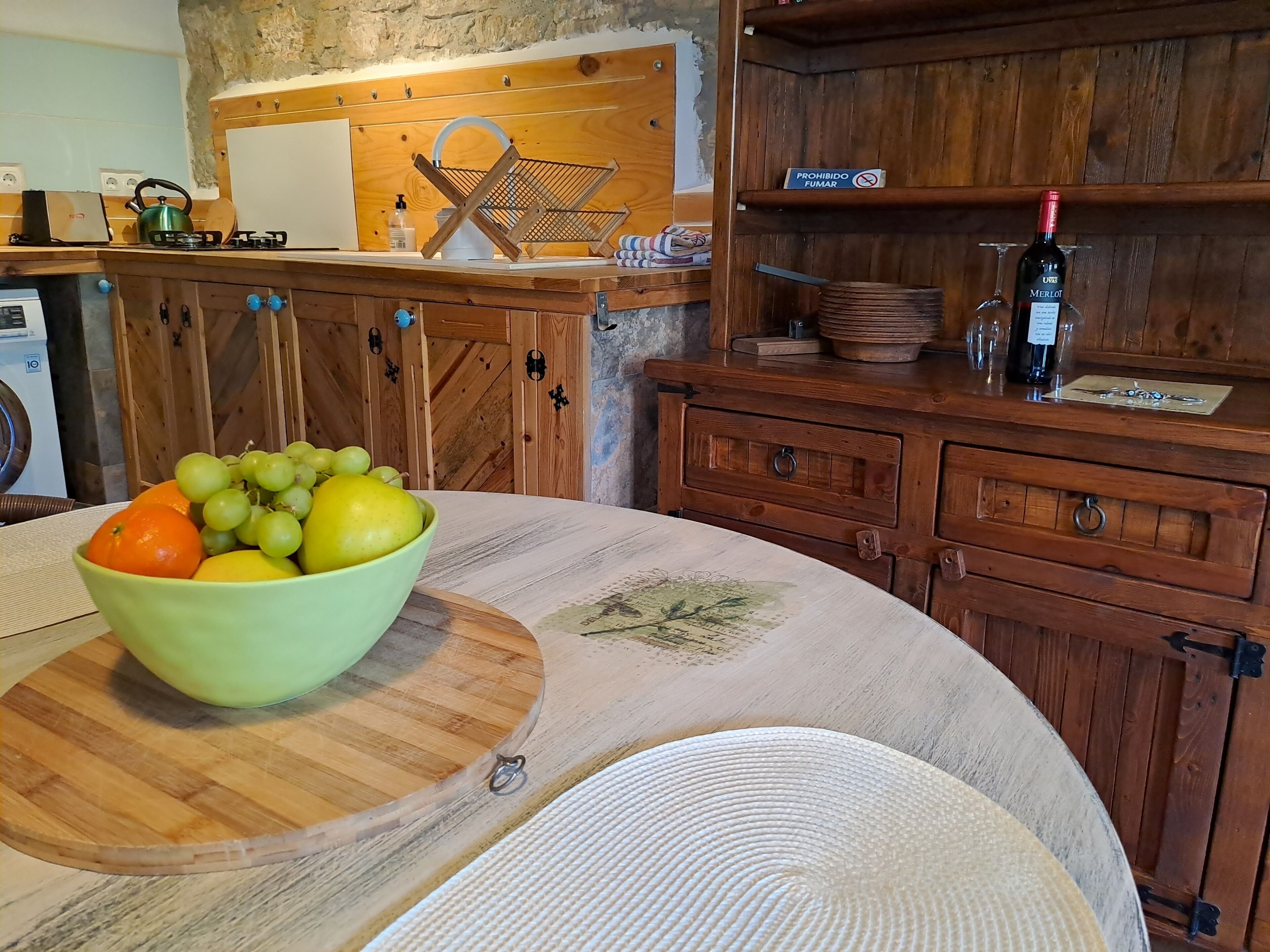 A kitchen with wooden cabinets, a fruit bowl on the counter, and a wine bottle on the shelf.