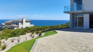 A modern two-story house with a balcony overlooking a coastal view.