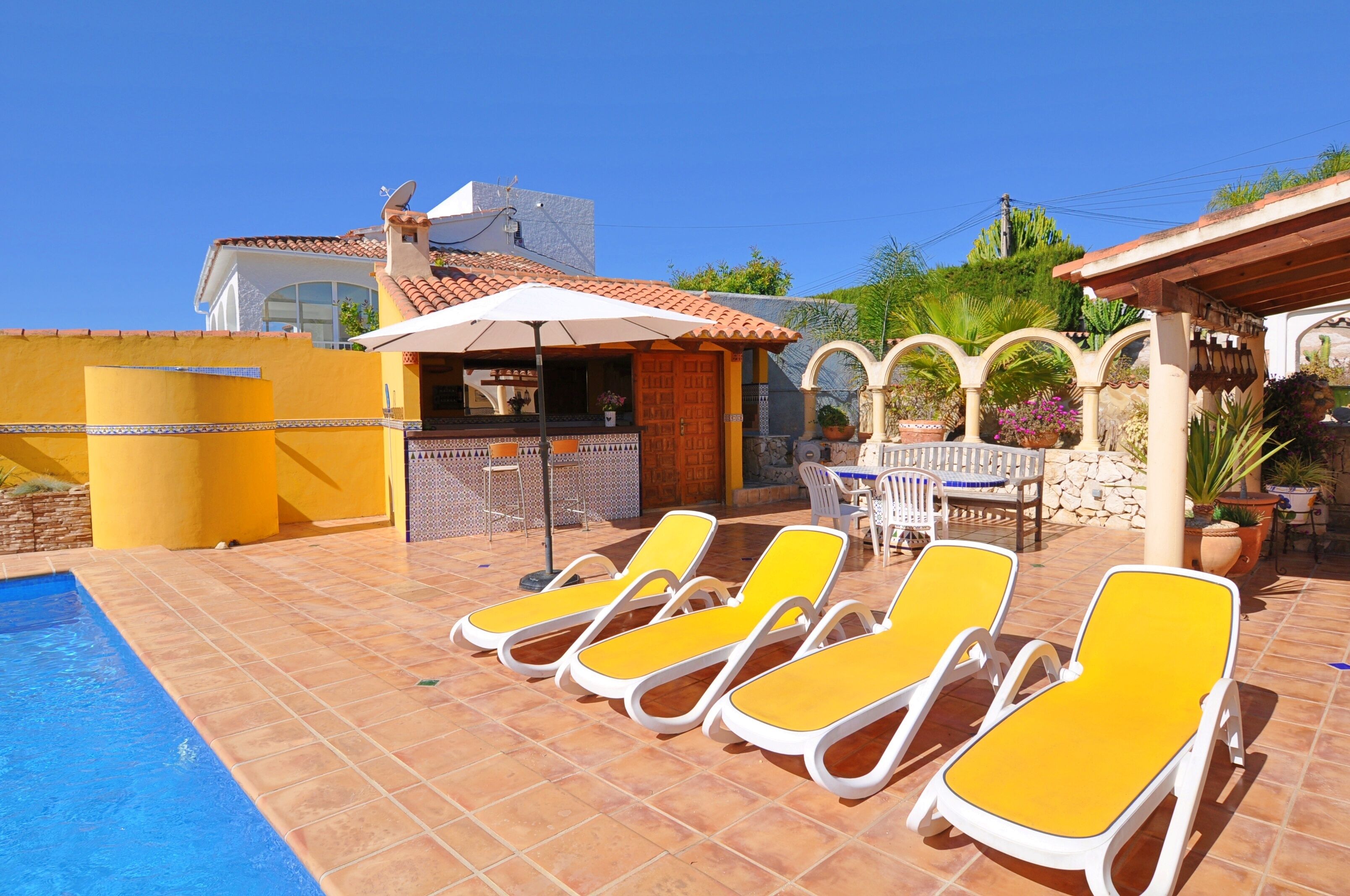 A pool area with sun loungers, a covered seating area, and a stone wall.