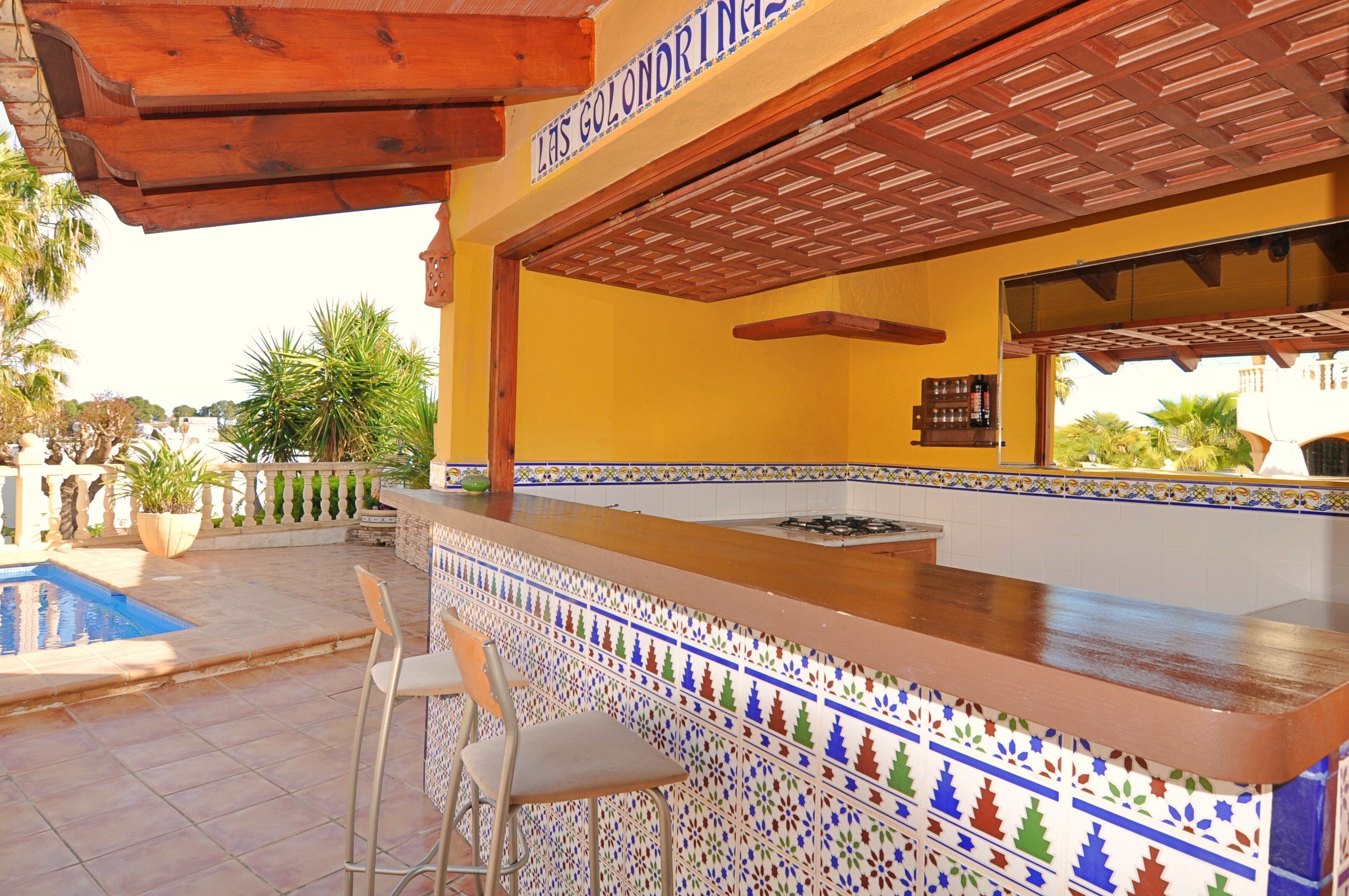 Eine Barbereich mit Fliesenrückwand, Barhocker und einem Pool im Hintergrund.