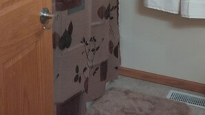 Ein Badezimmer mit Holztür, einer Duschvorhang mit Blattmuster und zwei weißen Handtüchern an der Wand.
