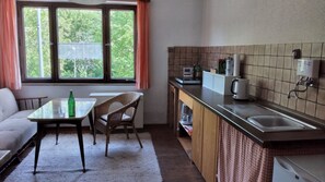 Une cuisine compacte avec un coin repas, une fenêtre avec des rideaux, une machine à café et un évier.
