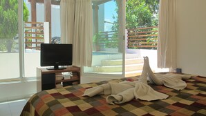 A hotel room with a bed, a television on a wooden stand, and a view of the outdoors through large windows. - Charming Penthouse, FREE INTERNET, CABLE and SAFE DEPOSIT BOX (Playa del Carmen)
