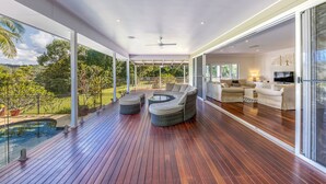 Un amplio espacio al aire libre con terraza de madera, jacuzzi y una zona de estar con sofás y televisor.