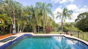 Una piscina con borde de azulejos, rodeada de una valla y palmeras.