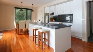 Cozinha moderna com uma ilha grande, armários brancos e vista para o verde lá fora.