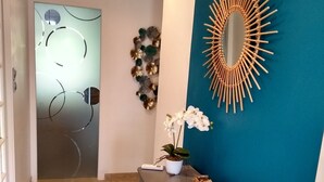 Ein Flur mit blauer Akzentwand, einem Spiegel in Sonnenstrahlform aus Holz, einer Topf-Orchidee und einem kleinen Tisch mit Pflanze und Behälter.