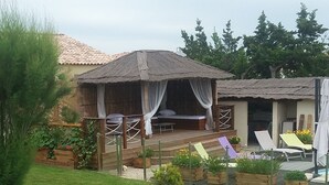 Ein gepflegter Garten mit Rasen, einer überdachten Sitzgelegenheit und verschiedenen Pflanzen in Töpfen.