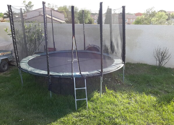 A trampoline with a safety net enclosure in a grassy yard. - A small piece of heaven (Restinclieres)