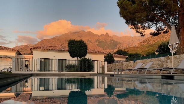 Ein Pool mit deutlicher Spiegelung der umliegenden Landschaft, darunter Berge und ein Gebäude mit einem Ziegeldach.