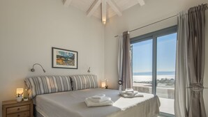 Camera da letto con un letto grande, un comodino, un quadro incorniciato e vista mare tramite una porta scorrevole in vetro.