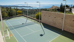 Un campo da tennis all'aperto con una rete, circondato da un muro in pietra e vista su un lago e montagne.