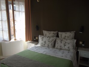 A bedroom with a bed, a nightstand, a wall-mounted lamp, and a window with curtains. - PRIME VIEW on OLD HARBOUR. Refurbished. Wifi, GARAGE on option, Cleaning +linen (Honfleur)