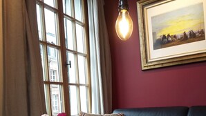 A living room with a black leather sofa, a glass coffee table with a vase of pink and red roses, a framed painting on the wall, and a hanging light bulb. - PRIME VIEW on OLD HARBOUR. Refurbished. Wifi, GARAGE on option, Cleaning +linen  (Honfleur)