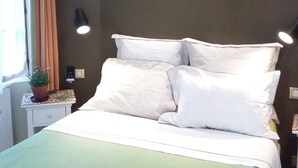 A neatly made bed with white bedding and pillows, a green throw blanket, a potted plant on a bedside table, and a wall-mounted lamp. - PRIME VIEW on OLD HARBOUR. Refurbished. Wifi, GARAGE on option, Cleaning +linen  (Honfleur)
