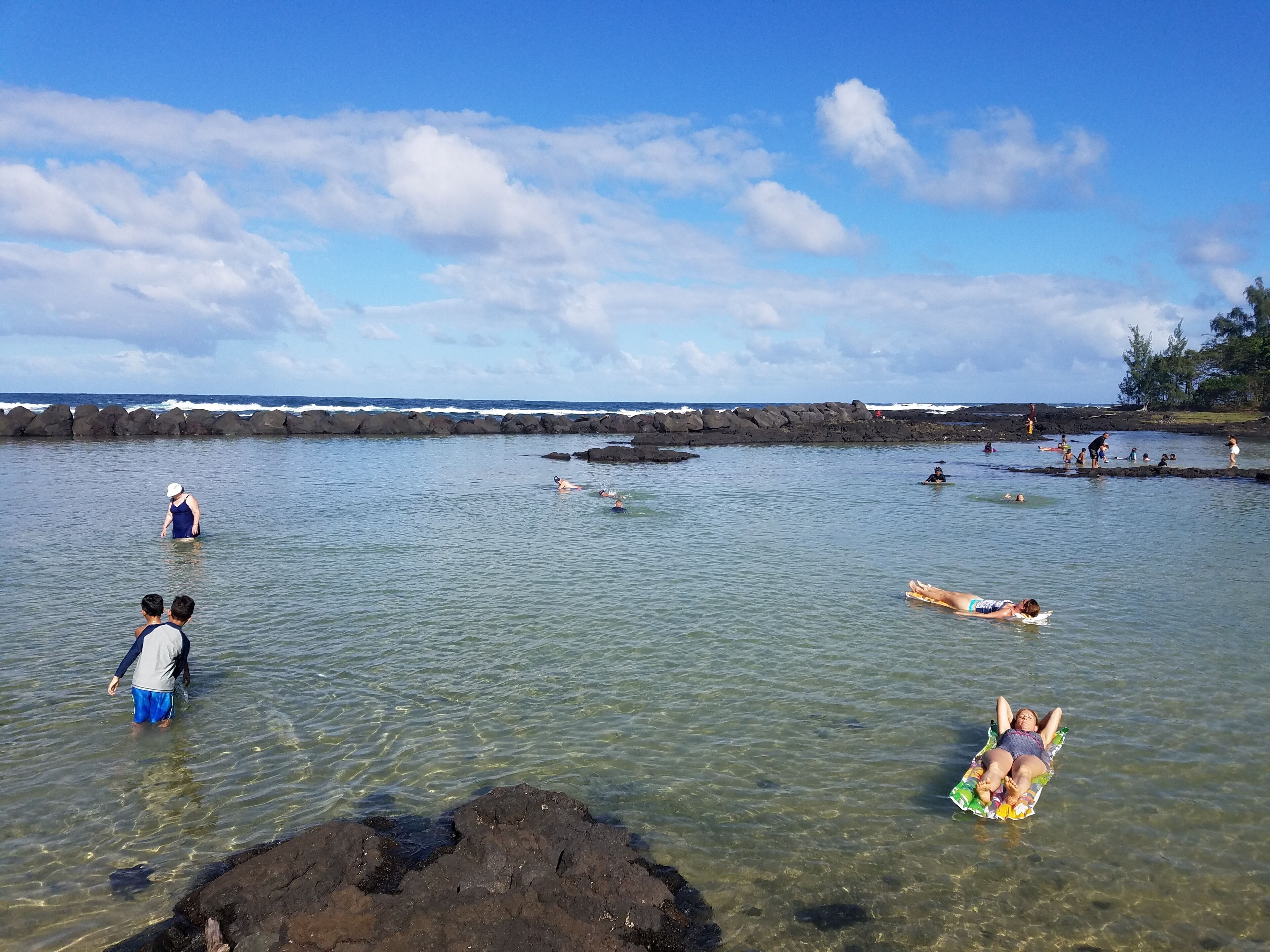 A beach scene with clear water, rocks, and people engaging in water activities.