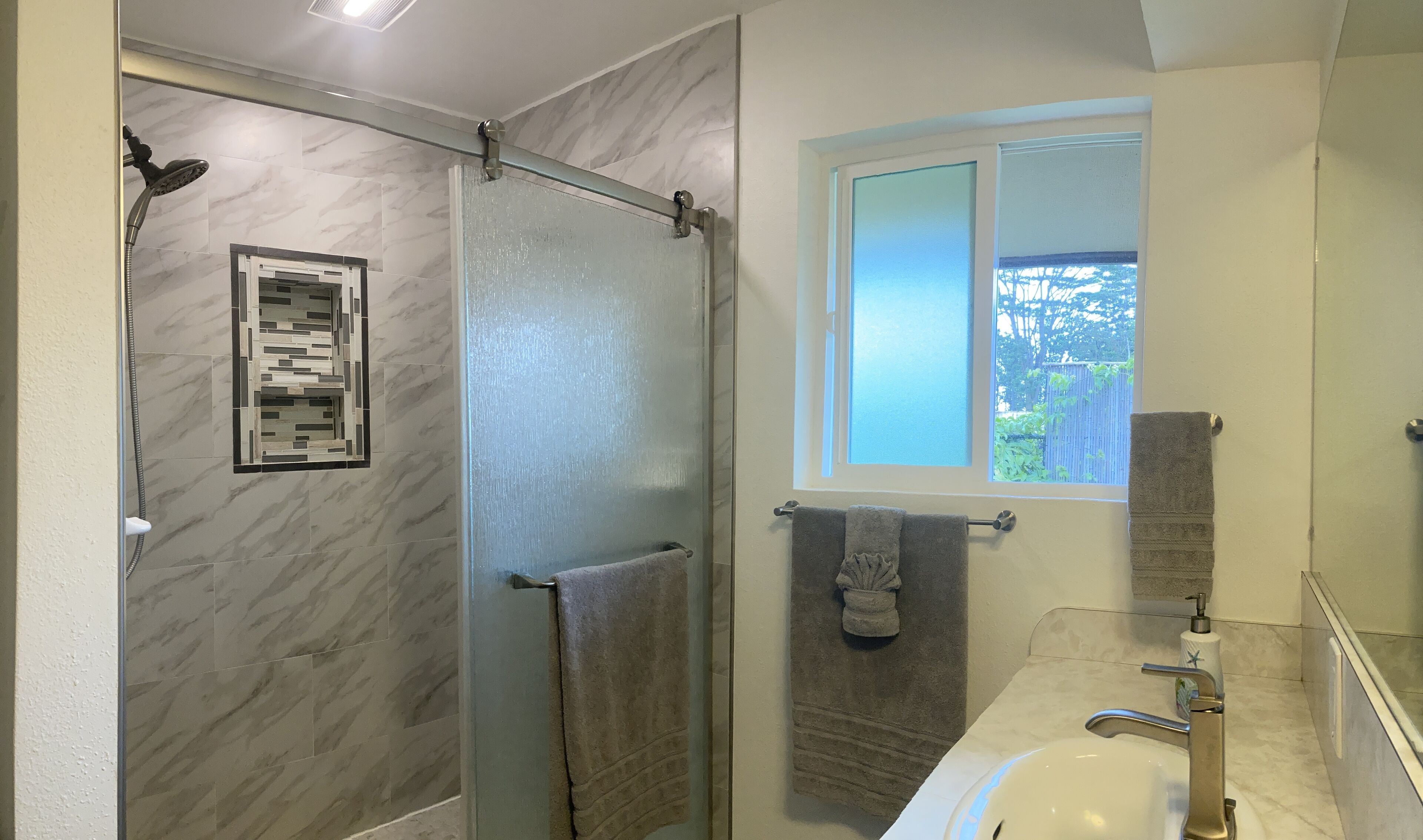 A modern bathroom with a glass-enclosed shower, a built-in vanity with a sink, and a window providing a view of greenery outside.