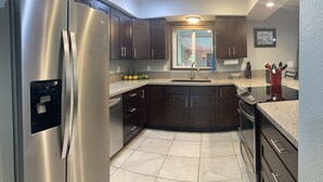 A modern kitchen with dark wood cabinets, stainless steel appliances, a granite countertop, and a window with a view of a building outside. - Spacious home in a lush green piece of paradise (Pahoa)