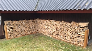 Ein überdachter Außenbereich mit Wellblechdach, einem Holzstapel und Rasenfläche.