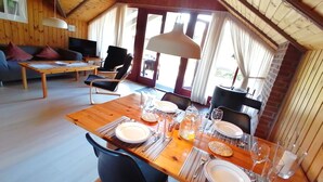 A dining area with a wooden table set for two, surrounded by chairs, in a room with wooden walls and a sloped ceiling. - Year-round relaxation in a Danish holiday home with a fireplace in Gartow am See  (Gartow)