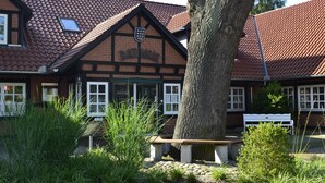 Ein traditionelles Gebäude mit Ziegeldach, einer hölzernen Bank und einem Baum im Vordergrund.