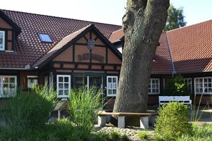 Un bâtiment traditionnel avec un toit en tuiles, un banc en bois et un arbre au premier plan.