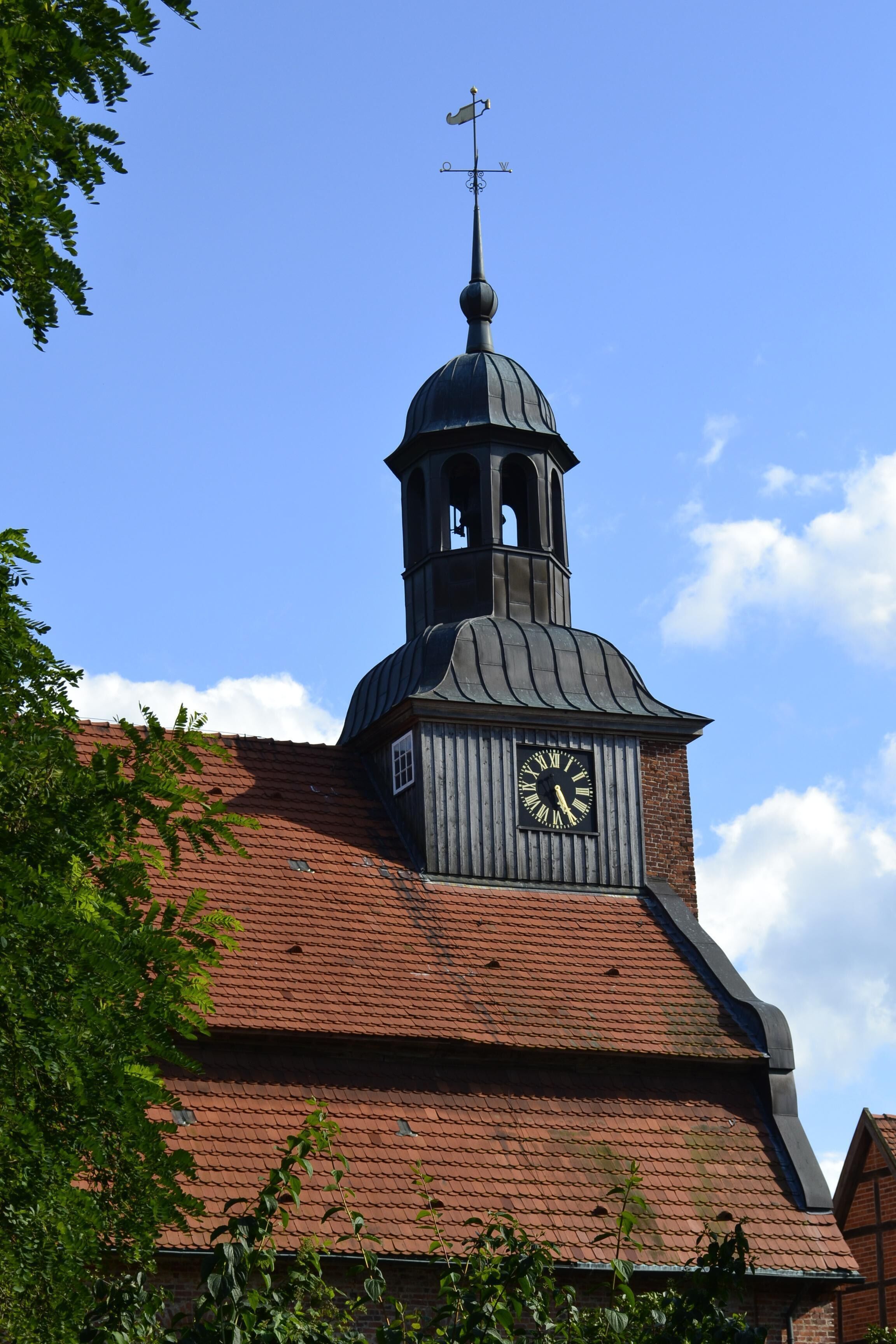 Uma igreja com uma torre do relógio e um indicador de vento.