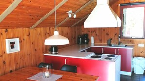 A cozy kitchen with wooden walls, a central island with a stove, and a dining area with a wooden table and chairs. - Year-round relaxation in a Danish holiday home with a fireplace in Gartow am See  (Gartow)