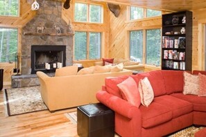 Cozy cabin interior with a stone fireplace, comfortable sofas, and a bookshelf filled with books.