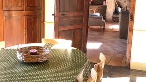 Une table à manger en bois, recouverte d’une nappe à pois verts, un panier en osier avec un couvercle rouge et une chaise.