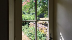 Une porte dotée d’une grande fenêtre divisée en quatre panneaux, qui offre une vue sur un jardin où l’on peut admirer des fleurs roses et de la verdure.