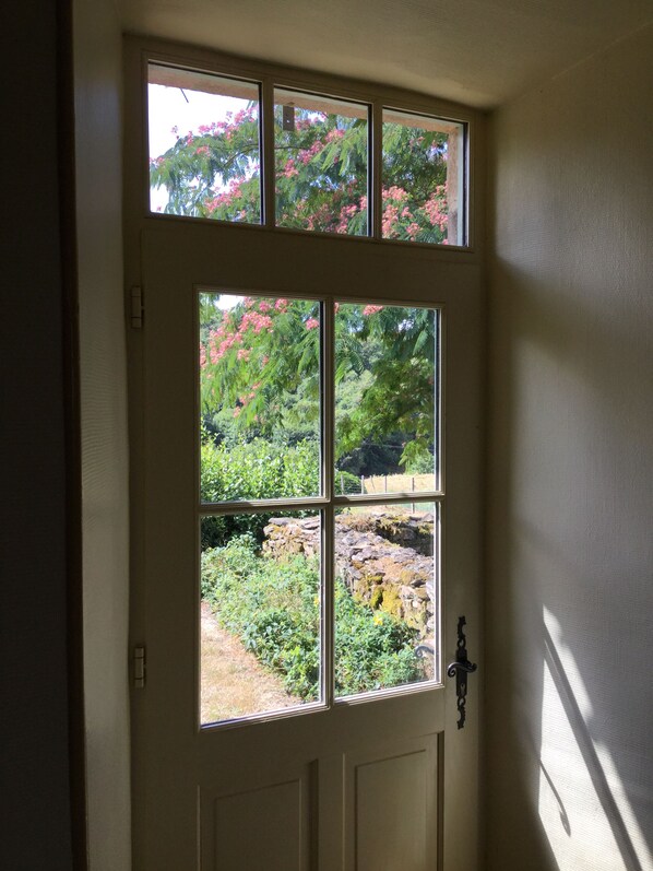 A door with a large window divided into four panes, offering a view of a garden with pink flowers and greenery. - Gîte des Chaises Basses - Typical house in Corrèze in absolute calm (Orgnac-Sur-Vézère)