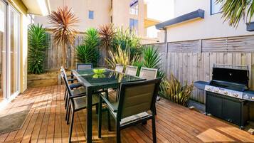 Eine Terrassengruppe im Freien mit Esstisch, Stühlen, Blumentöpfen und einem Grill.