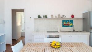 Une cuisine moderne avec des armoires blanches, un évier en acier inoxydable et un four encastré. On y trouve une table à manger avec un panier de citrons et une chaise.