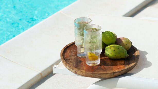 Une scène au bord de la piscine, avec un plateau contenant deux verres et quelques fruits.