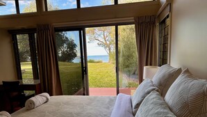 A bedroom with a large bed, a view of the outdoors, and a window with curtains. - Coast@Culburra -  newly renovated  - luxurious beachfront house with spa (Culburra)