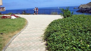 Ein gepflasterter Weg mit Metallgeländer, der zu einem Blick auf das Meer führt.