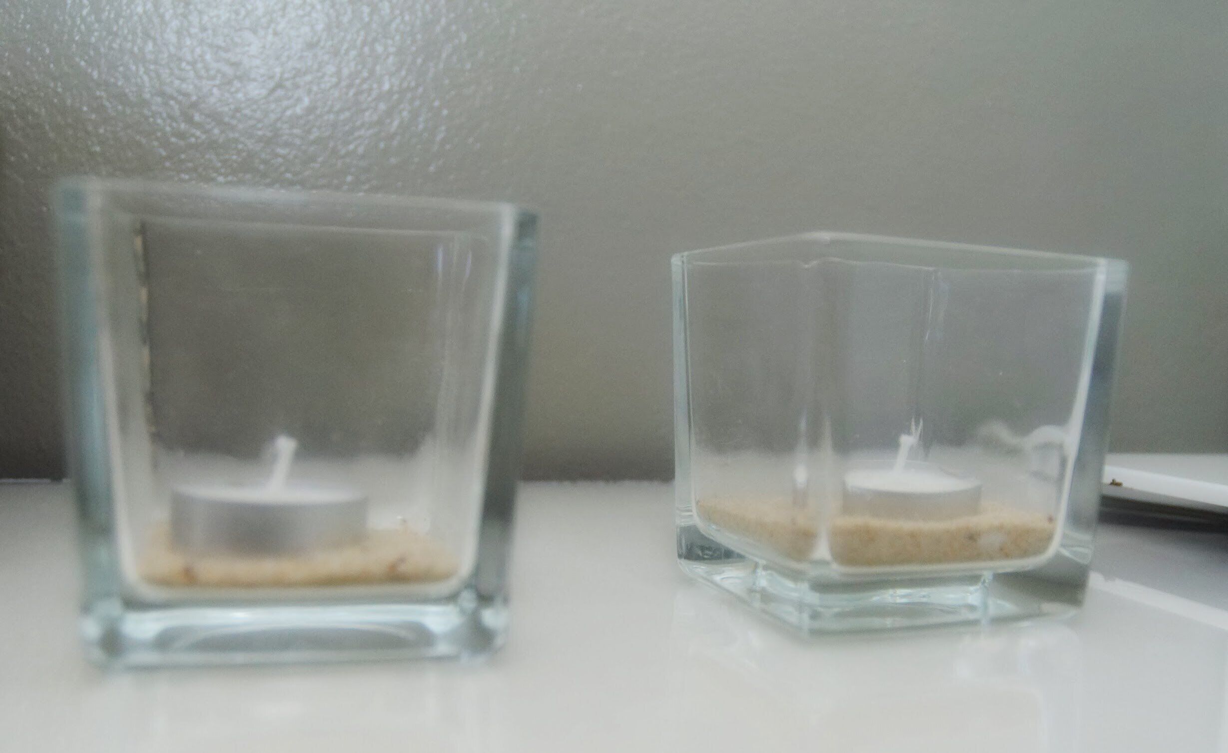 Two square glass candle holders with candles on a white surface.