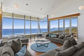 A modern living room with a large window overlooking the ocean, a round coffee table, and a sofa set.