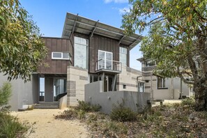 A modern two-story house with a flat roof, large windows, and a balcony.
