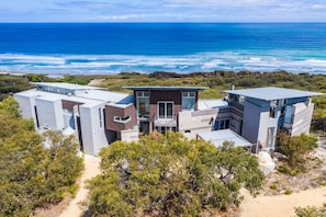 Une propriété côtière moderne comprenant plusieurs bâtiments, offrant une vue sur la plage et s’intégrant à un paysage naturel.