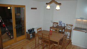 A compact kitchen with wooden cabinets, a dining table with chairs, a hanging light fixture, and a sliding glass door leading to a balcony.