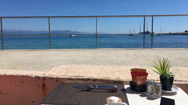 A table with a cup, salt and pepper shakers, a menu, and a plant, overlooking a marina with boats and mountains in the background. - "Côté Jardin" .... absolute calm in the center of Cannes ... with garage (Cannes)