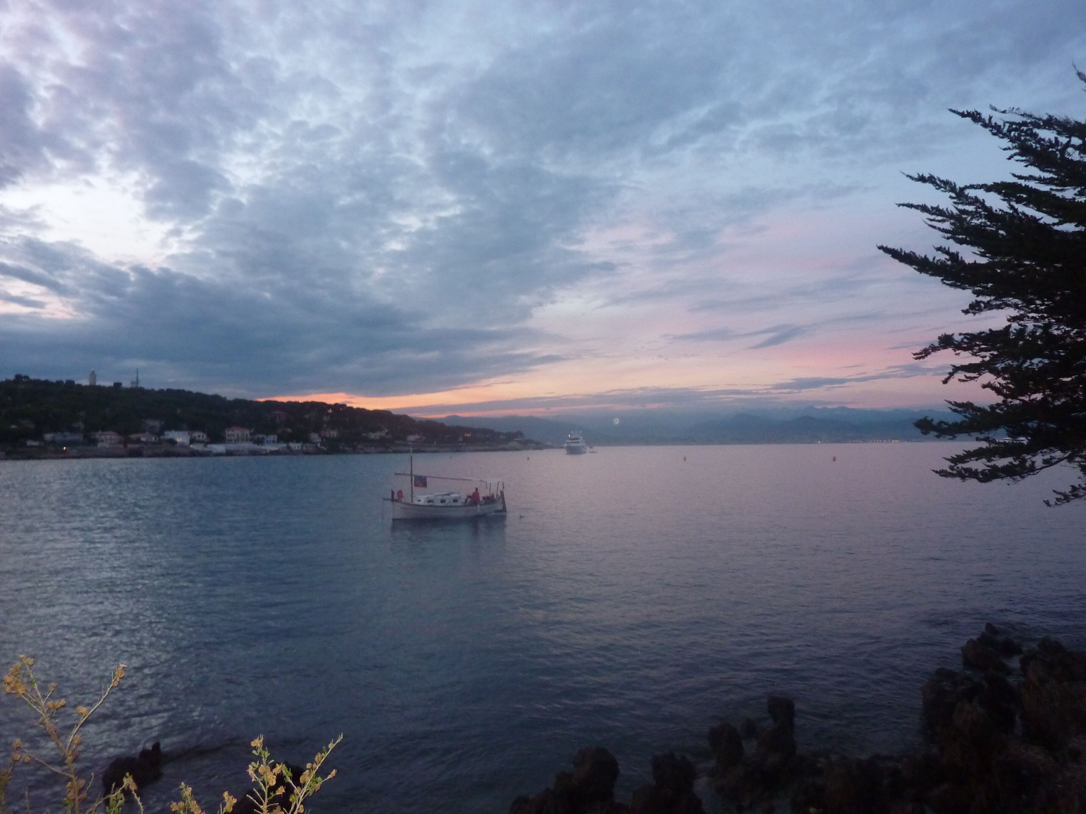 Une étendue d’eau calme, avec un bateau au centre, entourée d’un paysage vallonné et d’un ciel nuageux.