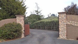 Une entrée fermée par un portail, avec des piliers en pierre et un portail en bois, le tout entouré de verdure et d’une clôture.