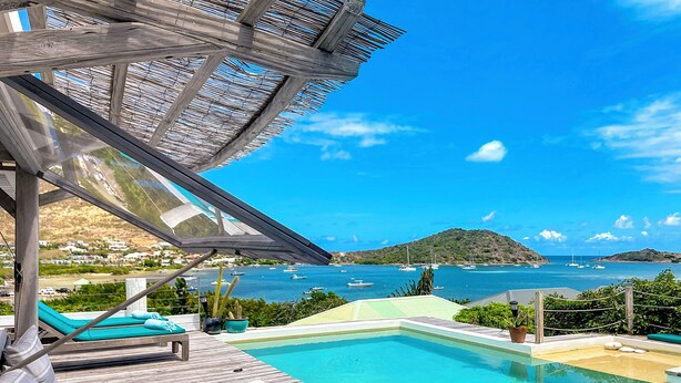 Une terrasse en bois avec une piscine, des chaises longues et une vue sur la mer et les collines.