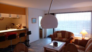A modern living room with a sofa, a coffee table, and a dining area with chairs and a kitchen counter. - Vacation apartment with a view of the North Sea (Schleswig Holstein)