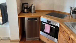 Uma cozinha compacta com máquina de lavar louça Bosch, forno, cafeteira e chaleira no balcão.