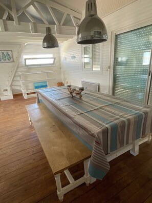 Um quarto com uma mesa de madeira, bancos e toalha de mesa listrada. Duas luminárias pendentes estão suspensas acima da mesa.