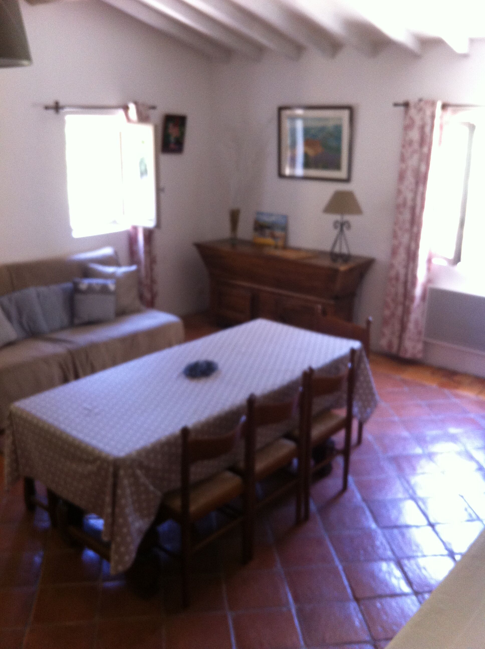 A dining area with a table and chairs, a sofa, a cabinet, and a window with curtains.